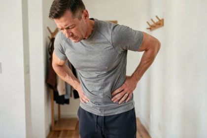 Homme tenant sa hanche droite et ses lombaires avec une expression de douleur, illustrant la douleur dans l'aine et les lombaires